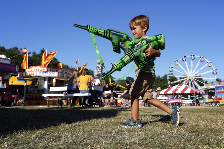Tucker Fochler, 5, of Gray, strides across the carnival grounds Friday at the 53rd annual Yarmouth Clam Festival with a pair of inflatable novelty rifles. Nonprofit organizations expect to serve more than 6,000 pounds of clams before the festival concludes Sunday evening.