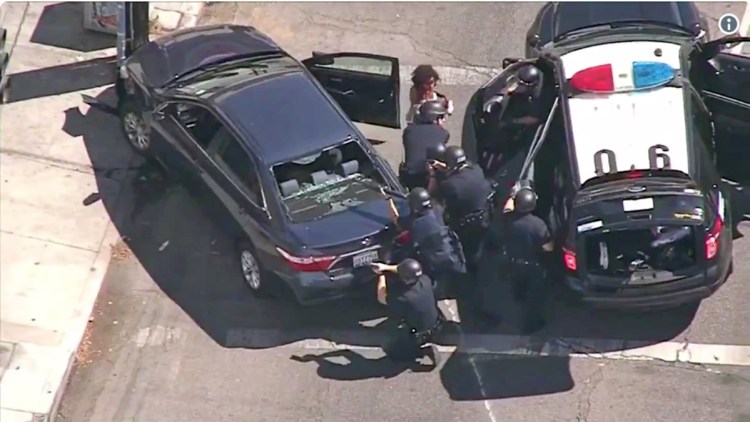 In this image from video, Los Angeles Police Department officers remove a passenger from a car that crashed after a pursuit with the driver, who ran into a nearby Trader Joe's supermarket in the Silver Lake district of Los Angeles on Saturday. He was later taken into custody after taking hostages at the store.