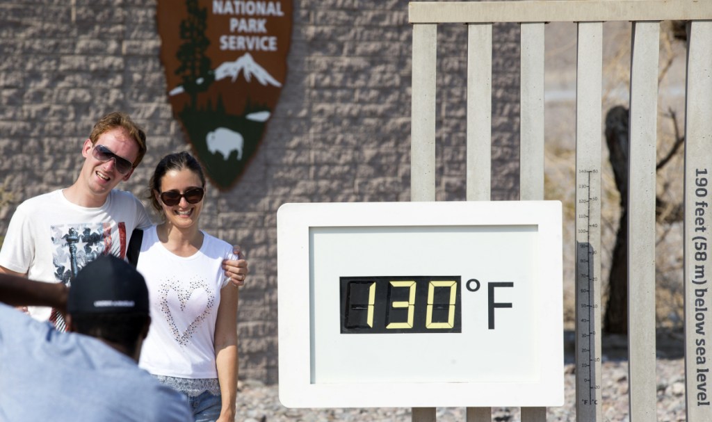 A couple poses at the Furnace Creek Visitor Center thermometer in Death Valley National Park, Calif., one of many areas experiencing record or near-record heat.