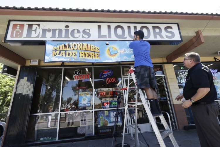 California Lottery official Mike Neis, right, watches as Amol Sachdev hangs a sign over his family's store Ernie's Liquors where a Mega Millions lottery ticket worth more than $500 million was sold in San Jose, Calif. 