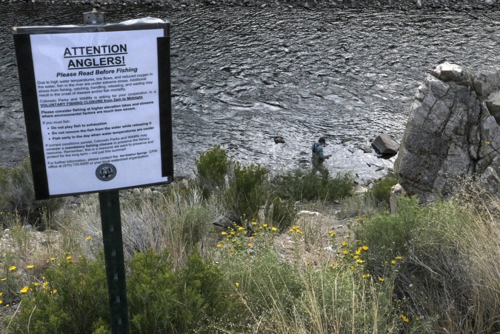 An angler makes his way along the Colorado River in late afternoon, despite the sign asking for cooperation with a "voluntary fishing closure" between 2 p.m. and midnight because water conditions have severely stressed fish.