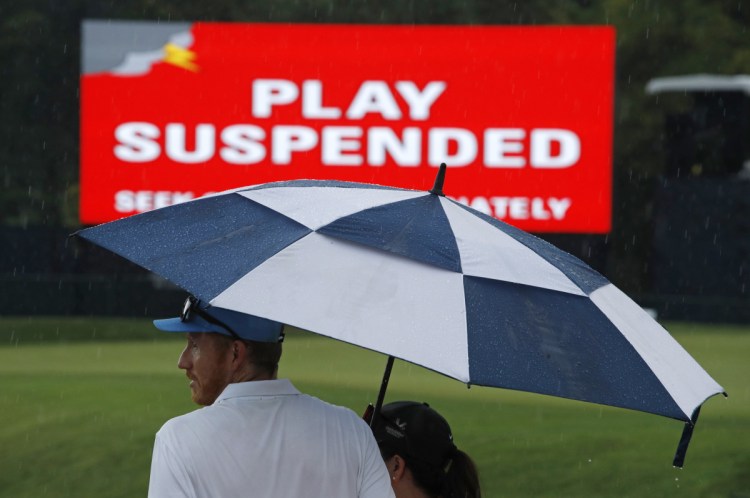 Patrons stand under an umbrella as play was suspended for the rest of the day during the second round of the PGA Championship golf tournament at Bellerive Country Club on Friday in St. Louis. Play was suspended due to heavy rain.