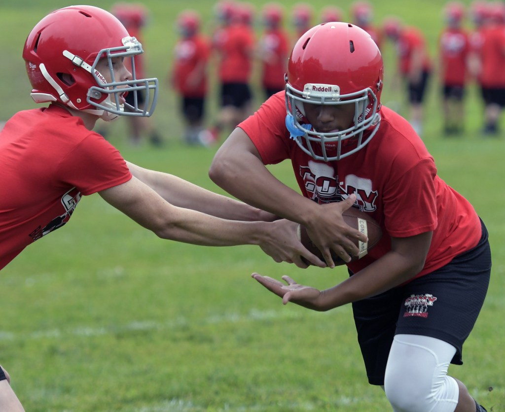 Cony High School football players work on a handoff during practice Monday morning in Augusta. Monday marked the first day fall sports teams could start practicing.