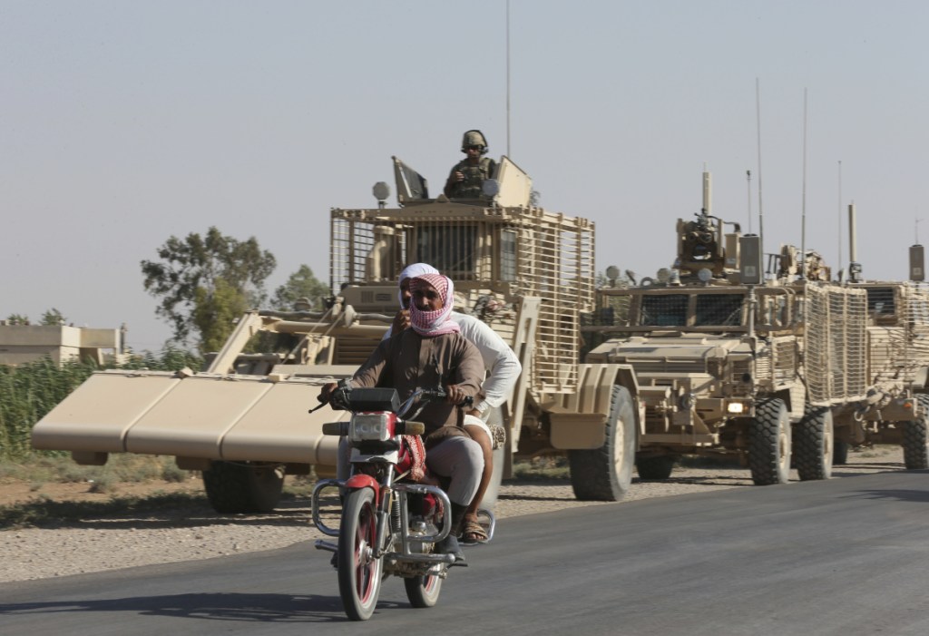 People ride past U.S. armored vehicles in Raqqa, Syria in July 2017. Figures obtained by the U.S. government and United Nations show The Islamic State may still have more than 30,000 militants in Syria and Iraq despite eradication attempts.