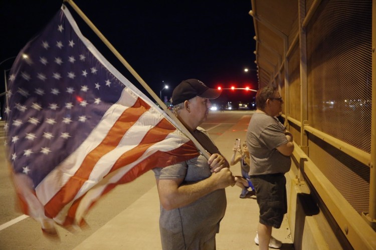 Joe Gruber, of Anthem, Ariz., holds an American flag at an overpass along Interstate 17 as he and dozens of others wait for the procession with the hearse carrying the late Arizona Sen. John McCain on Saturday night.