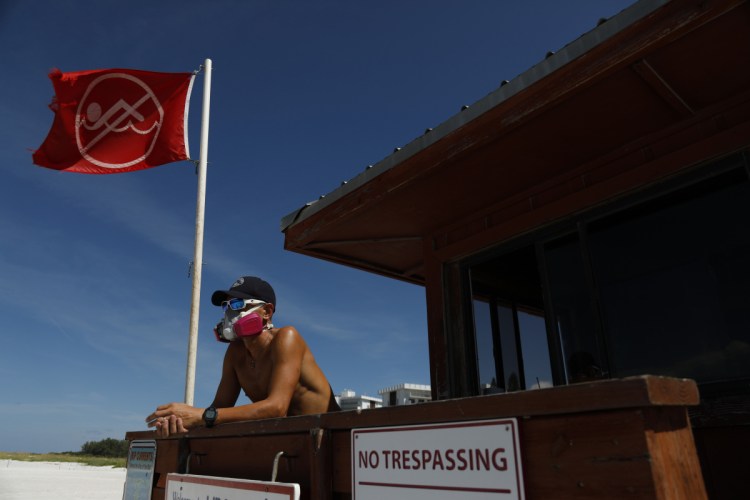 Sarasota County Emergency Services lifeguard Mariano Martinez wears a mask because of odor from the red tide at Lido Beach in Sarasota, Fla., where dead fish float in a nearby marina. Parts of Florida's Gulf Coast have been hit especially hard.