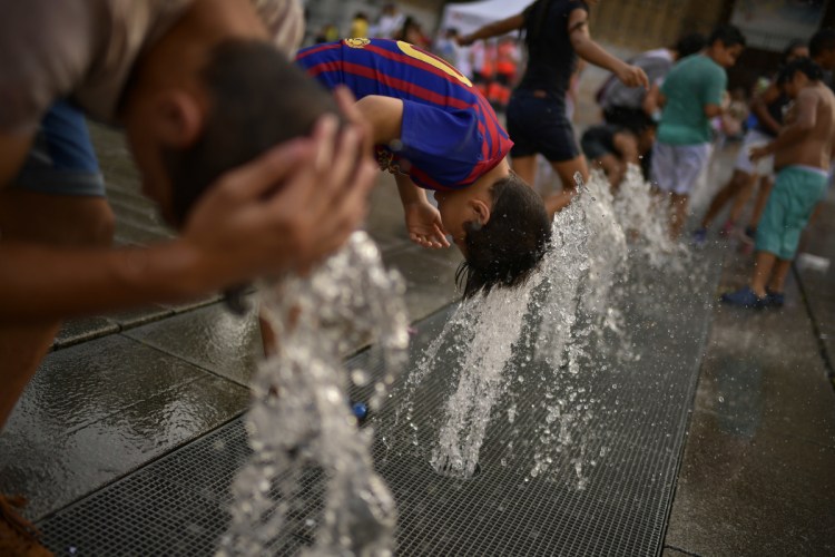 People cool off with water from a fountain  on Aug. 4 in Vitoria, northern Spain, where temperatures neared a record-breaking 115 degrees. A reader cites Europe's summer heat wave in noting that climate change is not just affecting "fringe areas."