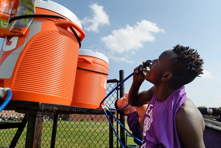 James Opio and Lucas Harbaugh, in background, drink water before the Deering High School football practice Tuesday. With Tuesday's hot weather, the team practiced without pads and took frequent water breaks.