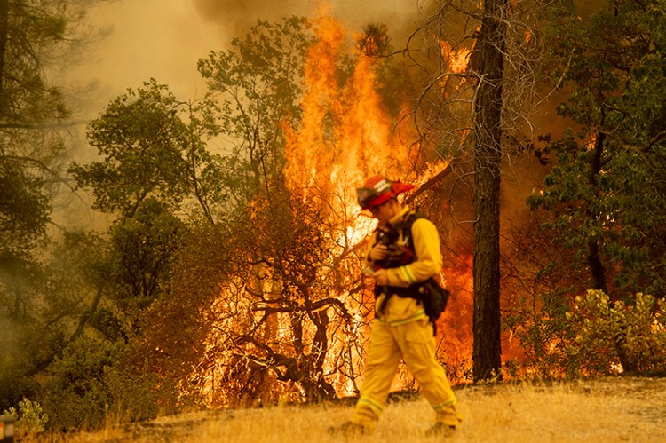 A firefighter walks near flames from the Carr Fire in Redding, Calif., on Saturday, July 28.