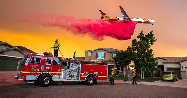 Firefighters use their hoses as a plane drops fire retardant on the Holy Fire behind homes in Lake Elsinore, Calif. on Wednesday.