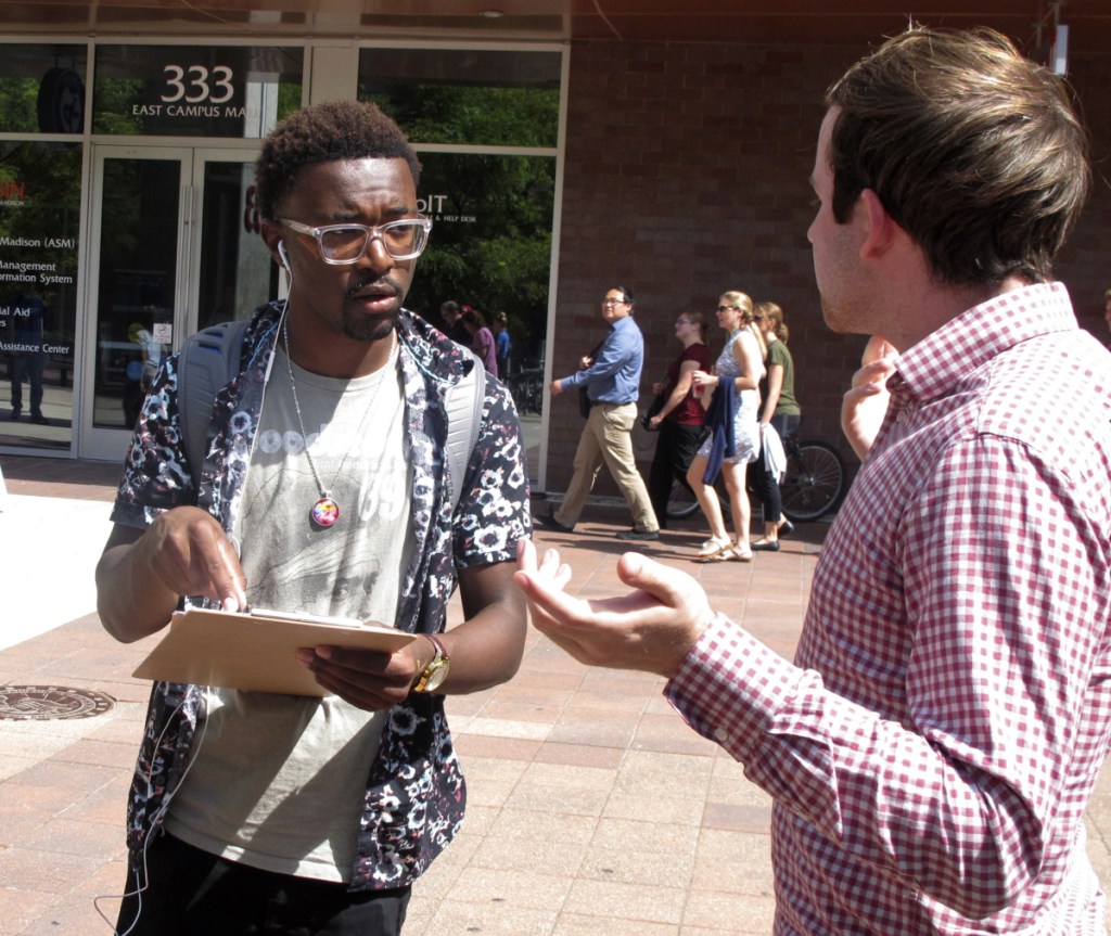 In this Thursday, Aug. 30, 2018 photo, University of Wisconsin freshman Kellen Sharp, left, gets information about registering to vote from NextGen America worker Sean Manning, right, in Madison, Wis. Sharp says he's excited to vote. He and others at the Madison event think young people are more energized than ever. (AP Photo/Scott Bauer)