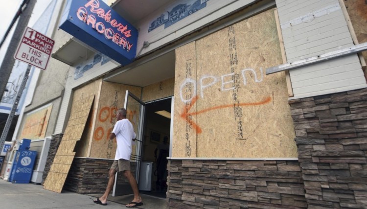 A man leaves the boarded-up Robert's Grocery in Wrightsville Beach, N.C., on Tuesday. Across the Carolinas, Virginia and Georgia, businesses are bracing for Hurricane Florence
