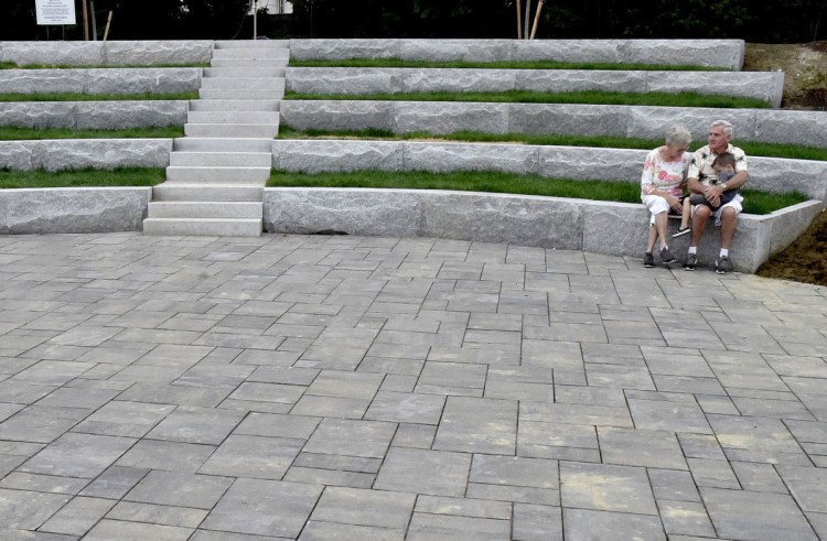 Donna and Leonard Dow and their grandson Owen rest on the steps of the granite amphitheater at the RiverWalk at Head of Falls in Waterville on Monday.