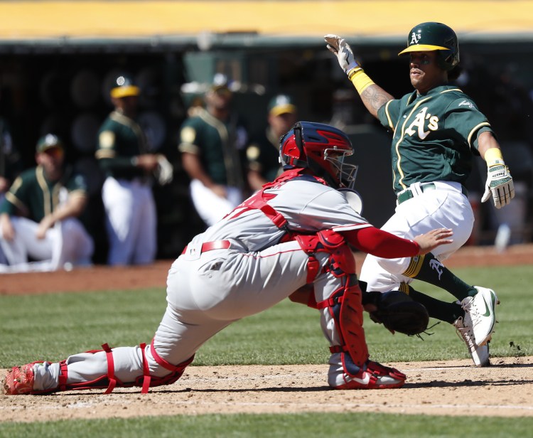 Oakland's Khris Davis slides past Angels catcher Francisco Arcia to score on a single by Stephen Piscotty in the fourth inning Thursday in Oakland, Calif. Later in the game, Arcia pitched the final two innings and allowed three runs as Oakland crushed Los Angeles, 21-3.
