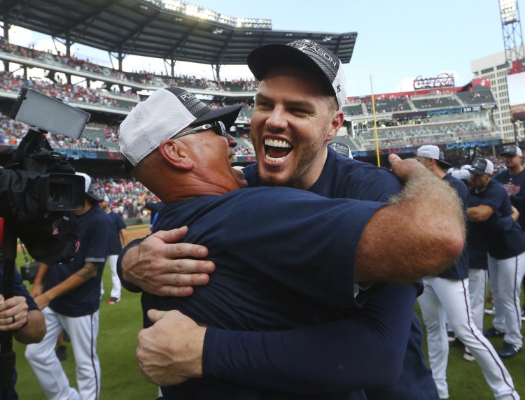 Atlanta first baseman Freddie Freeman, right, hugs Manager Brian Snitker after the defeated Philadelphia on Saturday to clinch the National League East Division.