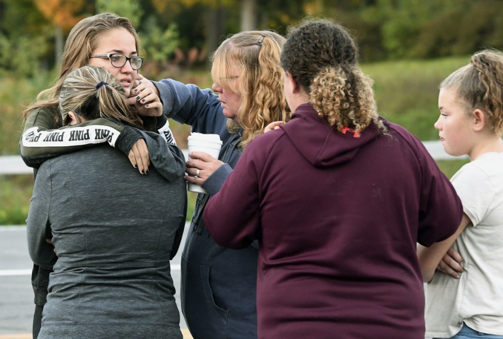 Friends of victims who died in Saturday's fatal limousine crash comfort each other after placing flowers at the intersection in Schoharie, N.Y., Sunday, Oct. 7, 2018. A limousine loaded with revelers headed to a 30th birthday party blew a stop sign at the end of a highway and slammed into an SUV parked outside a store, killing all people in the limo and a few pedestrians, officials and relatives of the victims said Sunday. 