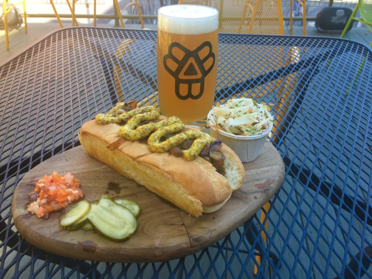 The vegan sausage at The Thirsty Pig comes covered in caramelized onions and spicy brown mustard. It is accompanied by vinegar coleslaw, Morse's Sauerkraut pickles and housemade hot carrot relish.