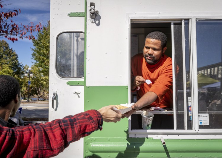 Isaak Gawo hands an order to a customer on Sunday. The Isuken Co-op truck has been making weekly trips to the Lewiston market. Most days though, it is parked on Sabattus Street in Lewiston, next to a farmstand operated seasonally by New Roots Cooperative Farm.