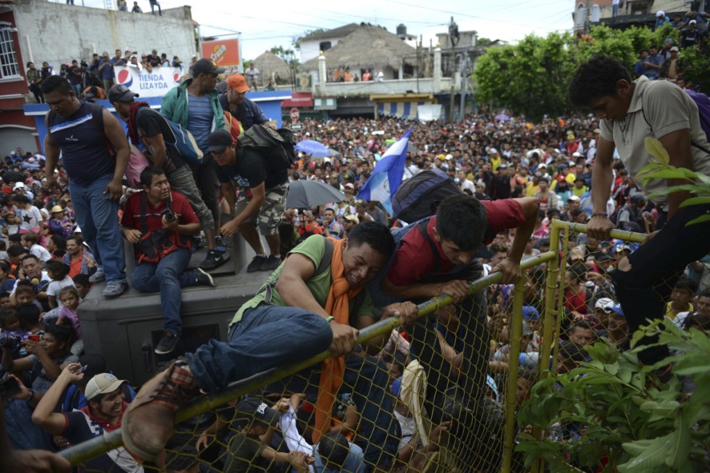 Thousands of Honduran migrants rush across the border towards Mexico, in Tecun Uman, Guatemala, Friday, Oct. 19, 2018. Migrants broke down the gates at the border crossing and began streaming toward a bridge into Mexico. After arriving at the tall, yellow metal fence some clambered atop it and on U.S.-donated military jeeps. Young men began violently tugging on the barrier and finally succeeded in tearing it down. (AP Photo/Oliver de Roos)