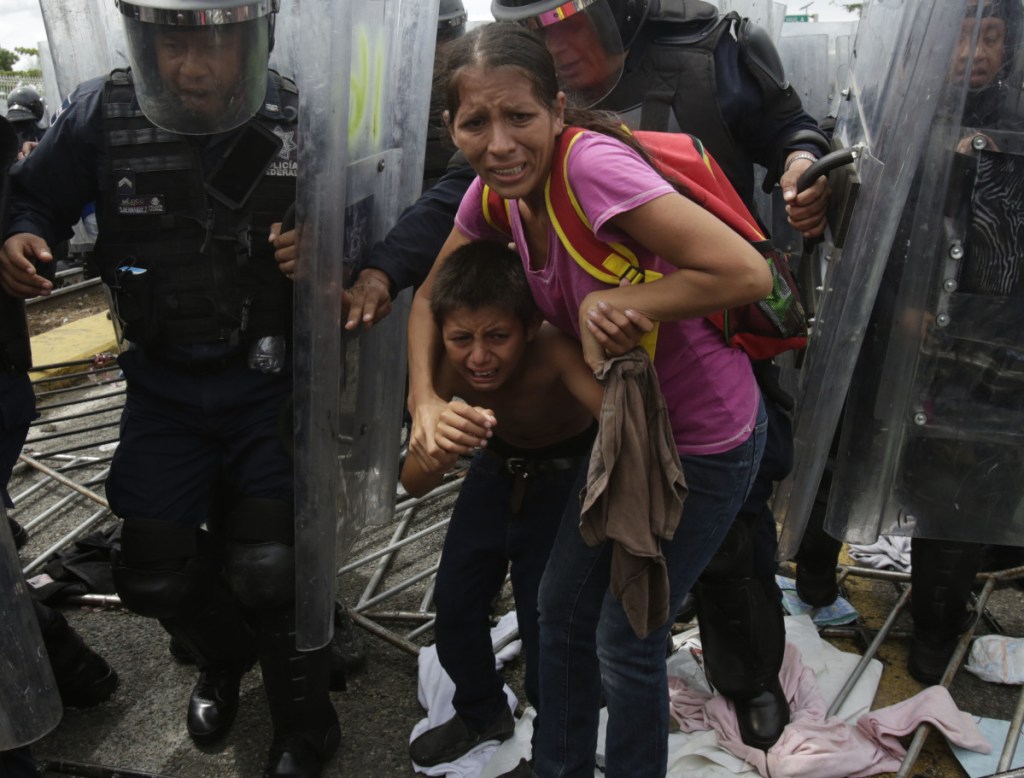 A Honduran migrant mother and her son are shielded by Mexican Federal Police from stones thrown by unidentified people at the border crossing in Ciudad Hidalgo, Mexico, on Friday.
