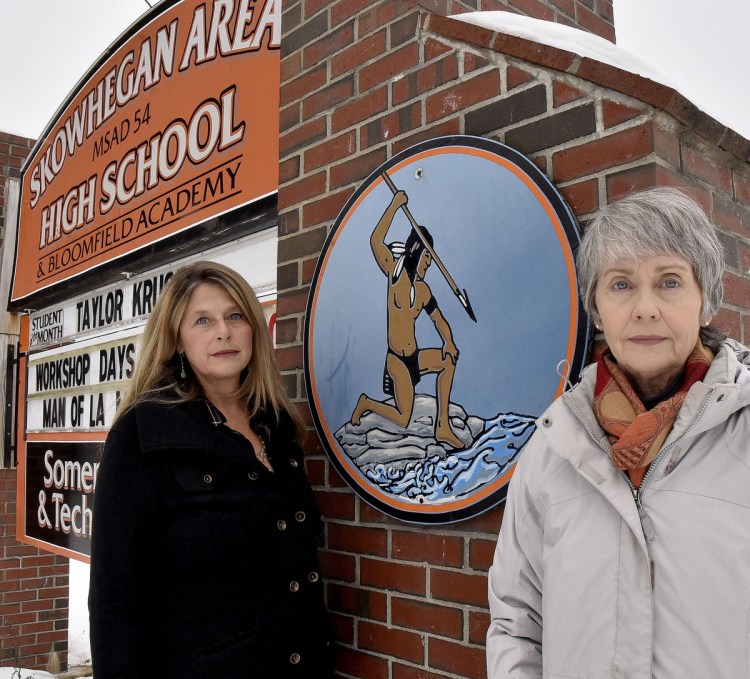 Hope Savage, left, and her sister, Lisa, stand beside the sign at the entrance to the Skowhegan Area High School that displays an image of a Native American on Monday. The Savages and others are urging the school board to cease using Indian as the school mascot.