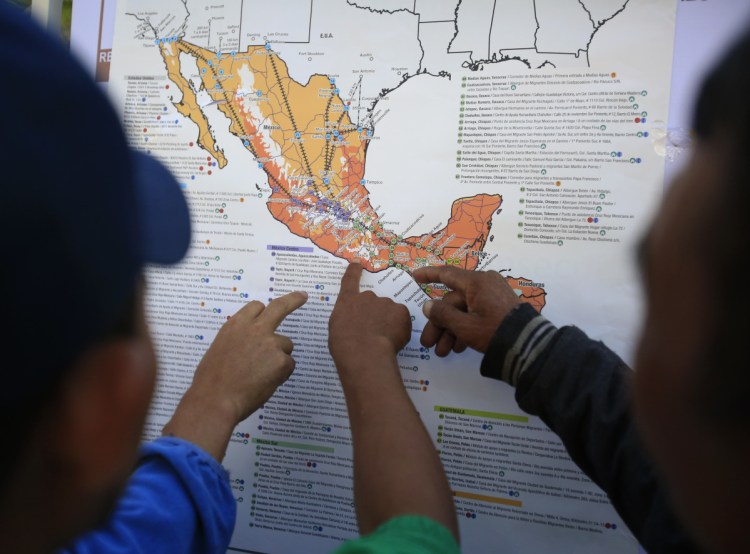 Migrants discuss their journey using a map posted inside the sports complex where thousands have been camped out for several days in Mexico City.
