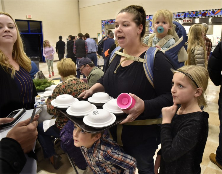 Rachael McKenney carries her youngest daughter, Olivia, while serving slices of pie, as her son, Liam, peers from under the tray at the Messalonskee Thanksgiving Day Community Meal on Thursday. McKenney's daughter Kaydence is at right and her sister Jenna Nesbit is at left.