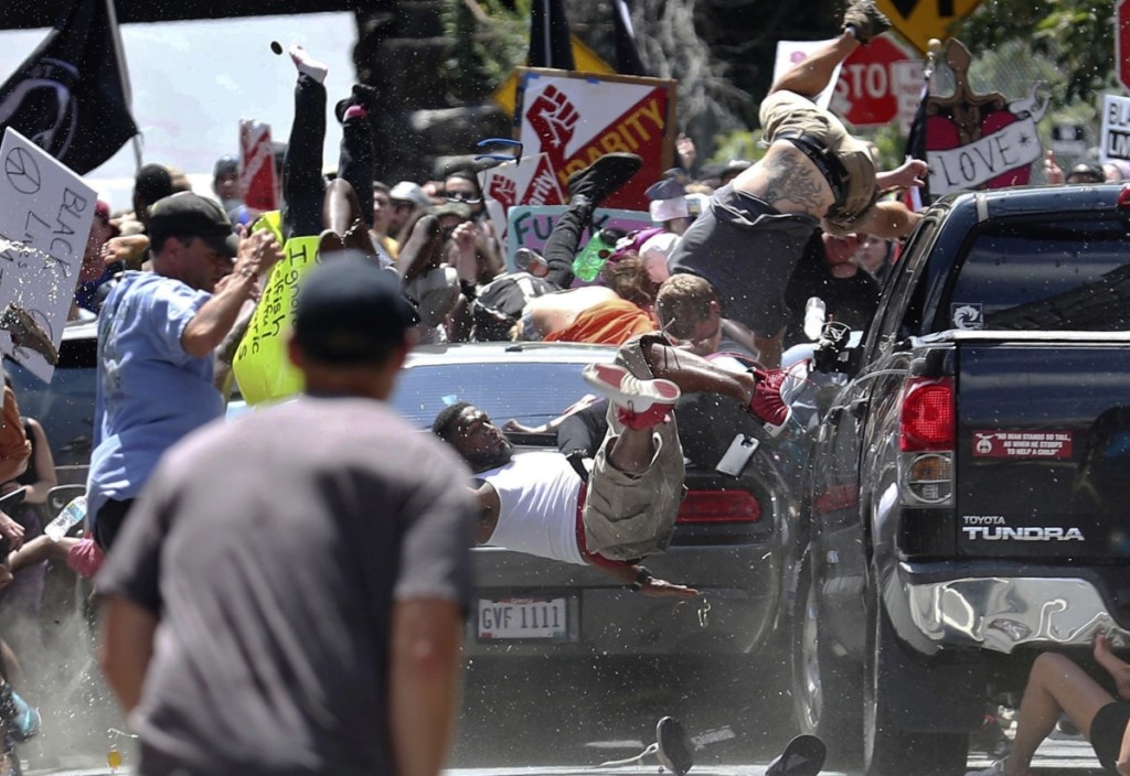 People fly into the air as a vehicle is driven into a group of protesters demonstrating against a white nationalist rally in Charlottesville, Va., on Aug. 12, 2017. James Alex Fields Jr. is accused of driving into the crowd, killing one person. At left, a protester holds a photo of victim Heather Heyer at a "Free Speech" rally in Boston.
Associated Press