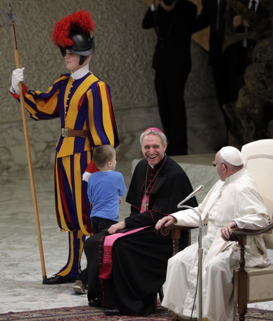 Pope Francis and Archbishop Georg Ganswein share a laugh as a child plays with a Swiss guard after getting up to the area where the pontiff was sitting during his weekly general audience at the Vatican.