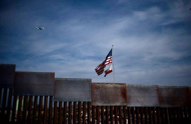 U.S. and California state flags fly behind the border wall, seen from Tijuana, Mexico, Monday, Nov. 19, 2018. Tensions have built as nearly 3,000 migrants from a caravan poured into Tijuana in recent days after more than a month on the road — and with many more months likely ahead of them while they seek asylum in the U.S. 