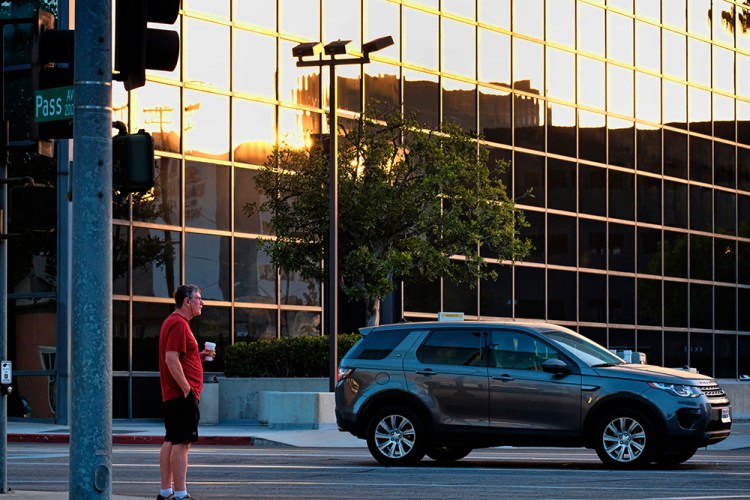 A man with his morning cup of coffee in hand crosses a street as the sun rises in the reflection of a building in Burbank, Calif. in September. This November, California voters will vote on Proposition 7 that would pave the way for year-round daylight saving time in the state. 