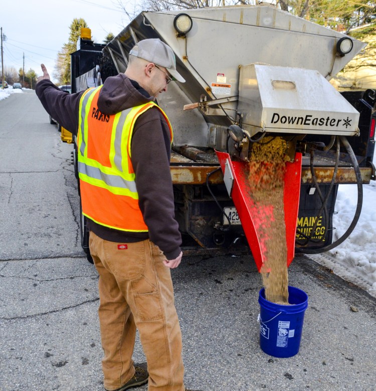 Ty Pelletier signals the truck's driver to stop flow of sand into a bucket Thursday in Augusta. City workers delivered or refilled buckets of sand to elderly or disabled residents' homes through the Augusta Age Friendly program.
