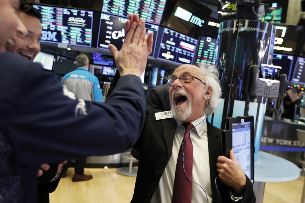 ABOVE: Trader Peter Tuchman, right, celebrates the record day for stocks before the closing bell Wednesday at the New York Stock Exchange. AT TOP: A board above the exchange floor shows the closing number for the Dow Jones industrial average.