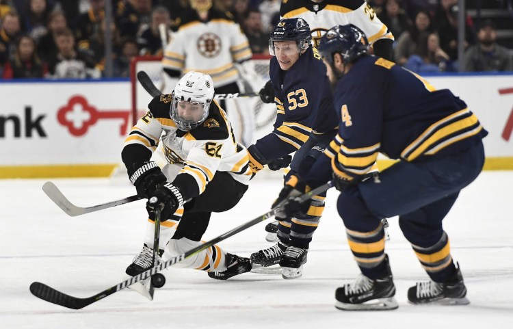 Boston center Sean Kuraly, left, reaches for a puck against Buffalo's Zach Bogosian, right, and Jeff Skinner during Saturday's game in Buffalo, N.Y. Kuraly scored in overtime to give Boston a 3-2 win.