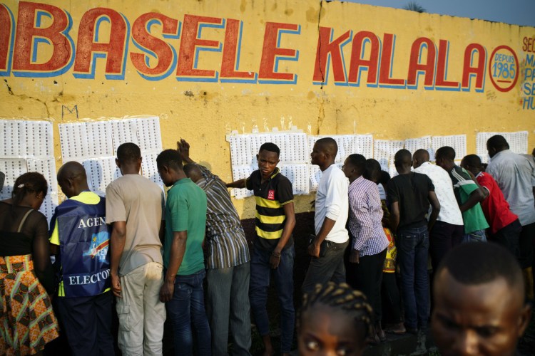 Election officials tape voter registration lists to the wall of a primary school in Kinshasa, Congo, as voters start to check their names Sunday. Forty million voters are registered for the presidential race.