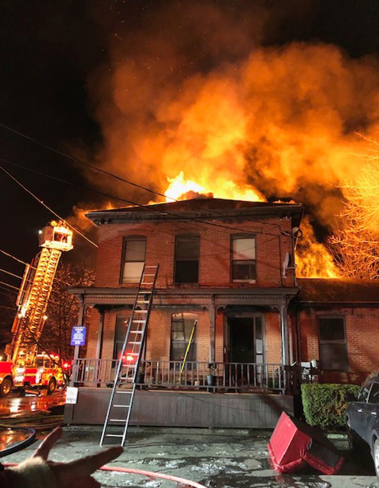 Fire shows through the roof of a building at 13 Pleasant Street in Westbrook on Sunday, December 30. The building housed a dentist’s office and had an apartment on the top floor that housed five people. 
