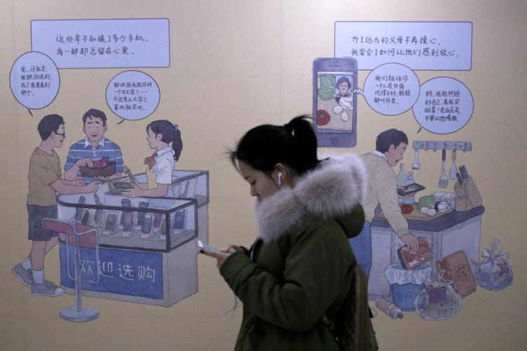 A woman uses an iPhone as she walks by a smartphone ad at a subway station in Beijing on Thursday. Apple’s slumping sales suggest that an era of increasing smartphone sales could be ending. Falling sales in China are a main factor, where consumers have a variety of cheaper options.