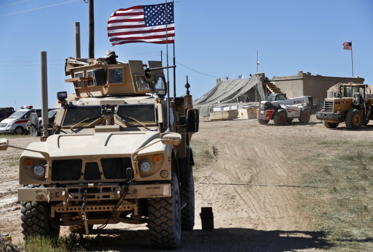 A U.S. soldier, left, sits on an armored vehicle behind a sand barrier at a position near the front line between the U.S-backed Syrian Manbij Military Council and the Turkish-backed fighters, in Manbij, north Syria in April 2018. 