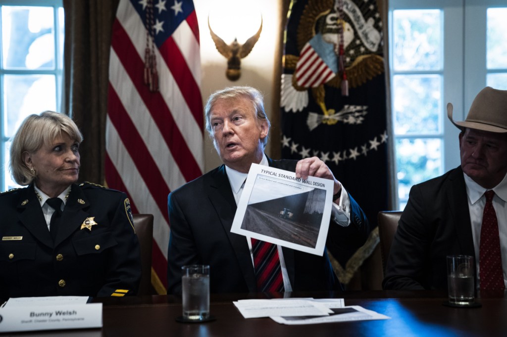 President Trump holds up a photo of a "typical standard wall design" as he speaks during a roundtable discussion on border security with administration officials at the White House on Friday.