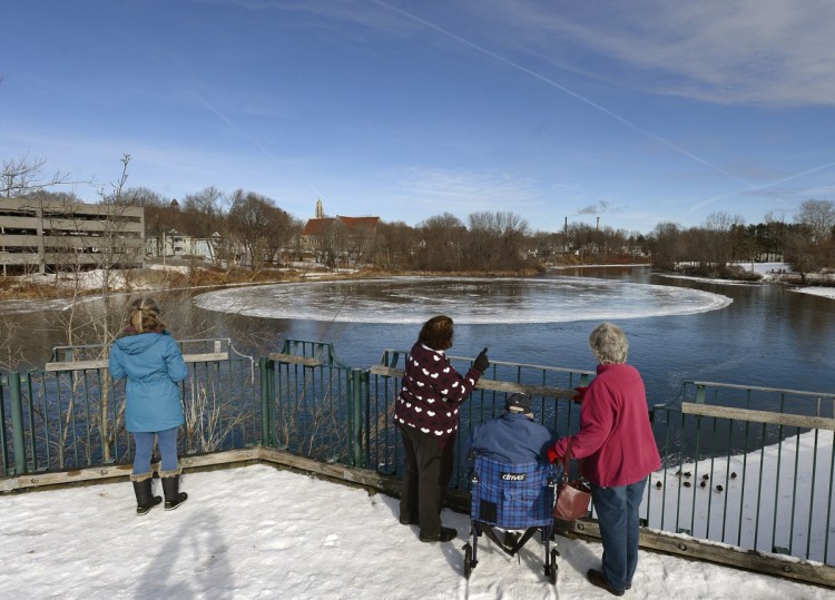 Curious observers watch the rotating disk of ice Tuesday on the Presumpscot River in Westbrook. One theory of how it formed: The flow of the river is pushing the ice disk along like a paddle wheel as ice builds up on the edges.