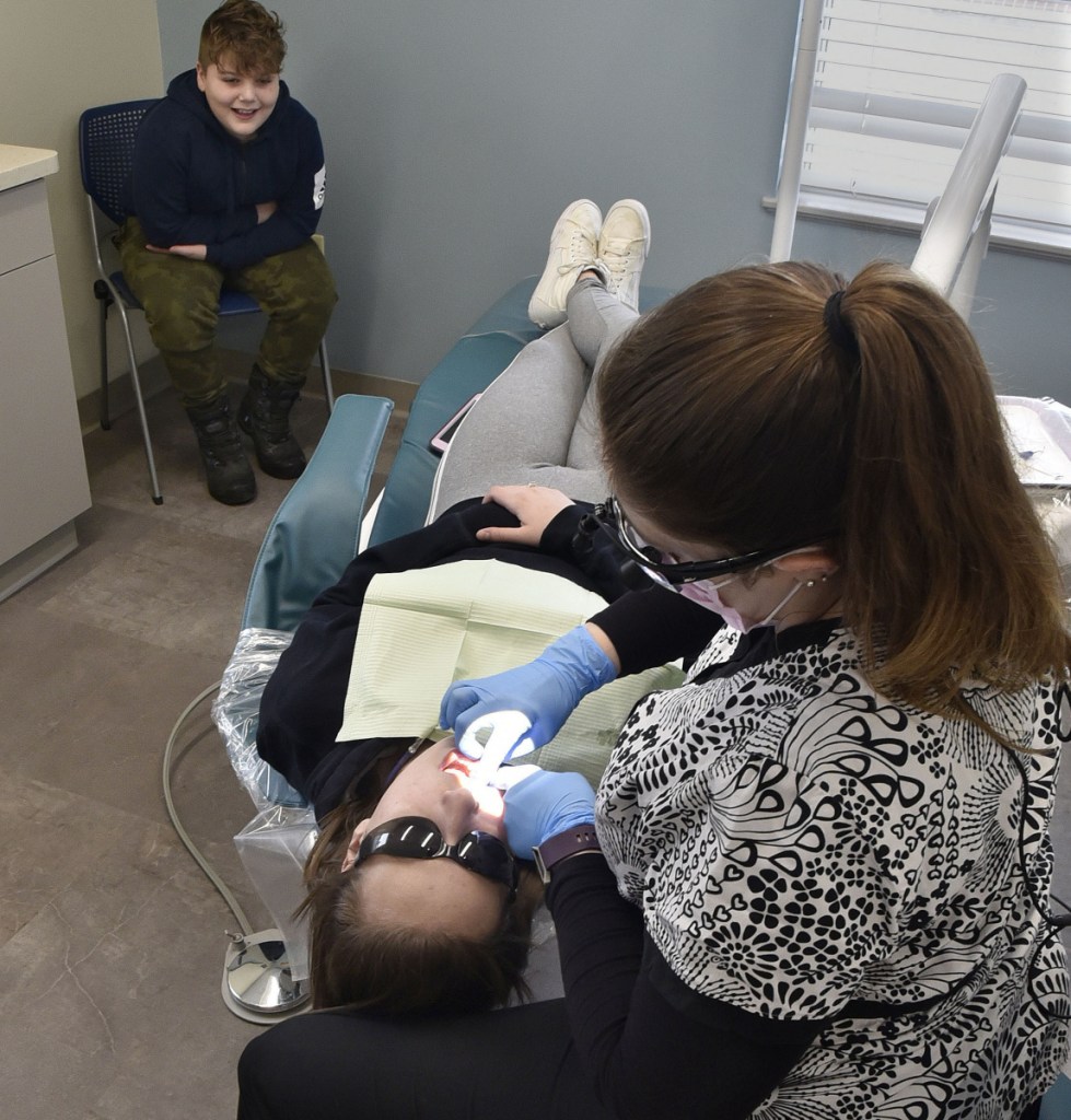 Paige Blake-Ireland cleans the teeth of Theresa Mansfield as her brother Landen Grip waits his turn at the new Waterville Community Dental Center at FirstPark in Oakland on Wednesday.