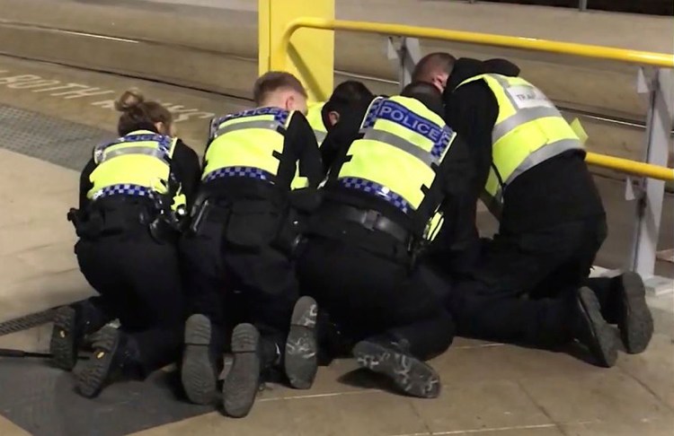 Police restrain a man accused of stabbing three people at Victoria Station in Manchester, England, late Monday.