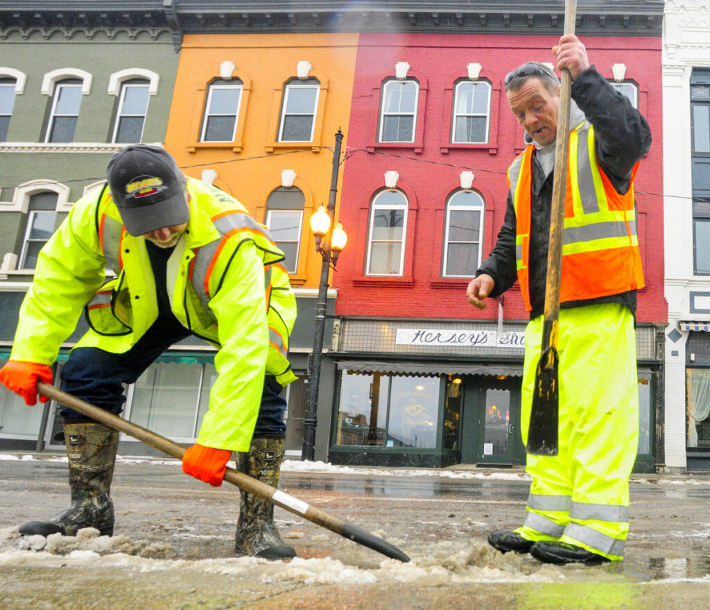 Augusta Public Works employee Rick Allen, left, shovels up pieces of ice that Lee Edwards chopped off a Water Street storm drain on Thursday in downtown Augusta. The warm, rainy weather had state and local crews out clearing drains to avoid flooding. 