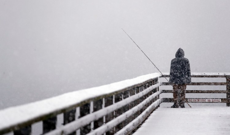 Hershel Odle looks out toward the cityscape lost in a whiteout as he fishes from a pier during a snowstorm Friday in Seattle. More than a foot of snow was recorded in some areas, including on the Olympic Peninsula.