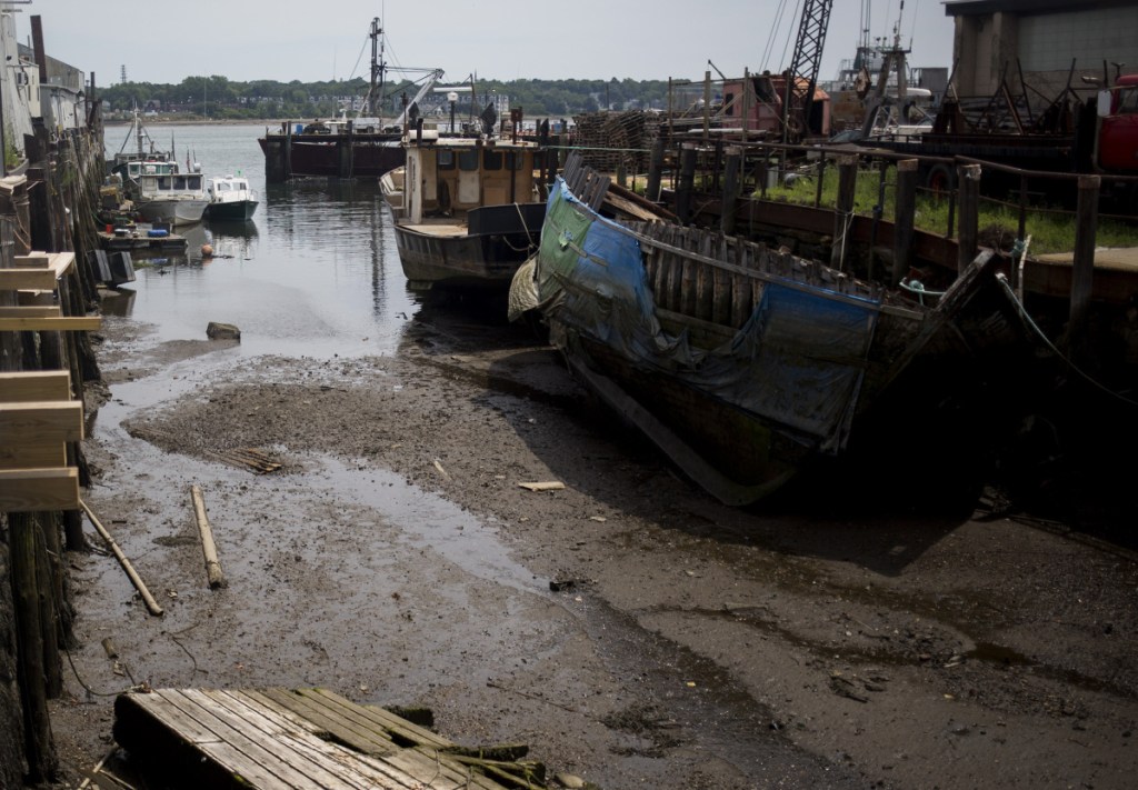 PORTLAND, ME - JULY 28, 2016: Boats lie in silt during low tide at Sturdivant's Wharf along Portland Harbor. Numerous public and private wharves have lost valuable berthing spaces as silt carried down the Fore River and from occasional sewer and stormwater runoff has built up around them.