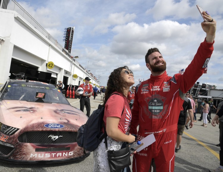 Corey LaJoie, right, poses for a selfie with Jenny Schnell in front of his car during a practice session Saturday for the Daytona 500. Lajoie, one of the eight Daytona rookies, has his face painted on the hood of his car.