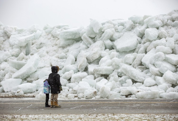 Local residents check out a massive buildup of ice that was pushed onto the shore of Mather Park in Fort Erie, Ontario, Canada, on Monday. A wind storm Sunday broke an ice boom in Lake Erie and allowed the ice, which was floating on the water at the mouth of the Niagara River, to spill over the retaining wall and onto the shore and the roadway above.