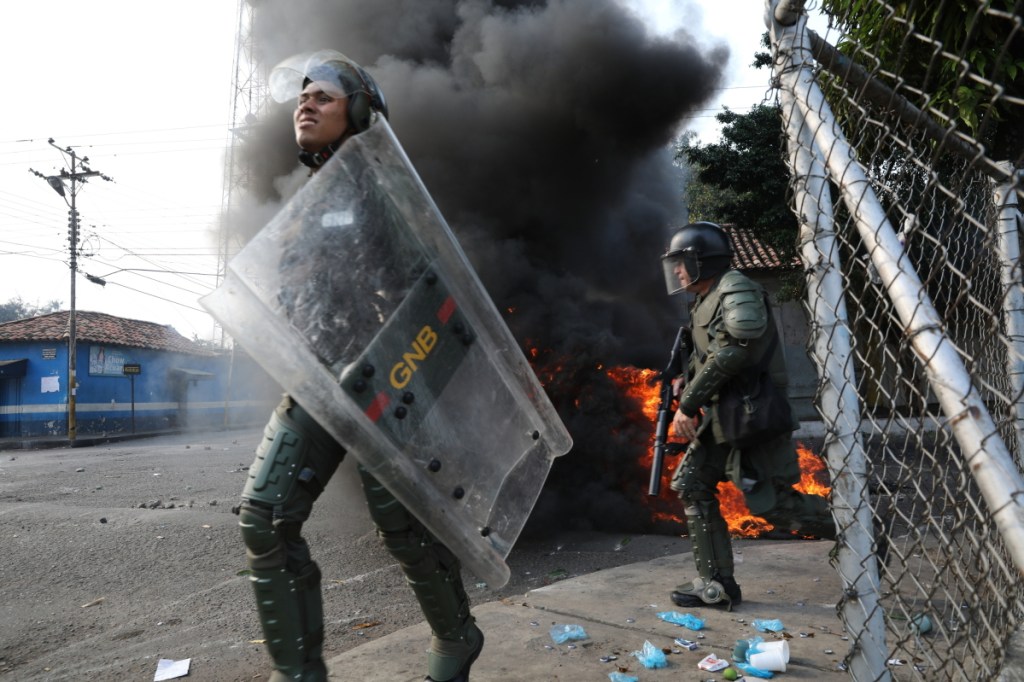 Officers of the Bolivarian National Guard run Saturday during a clash with residents who cleared a barricaded bridge while trying to bring humanitarian aid into Venezuela in Urena, near the border with Colombia.