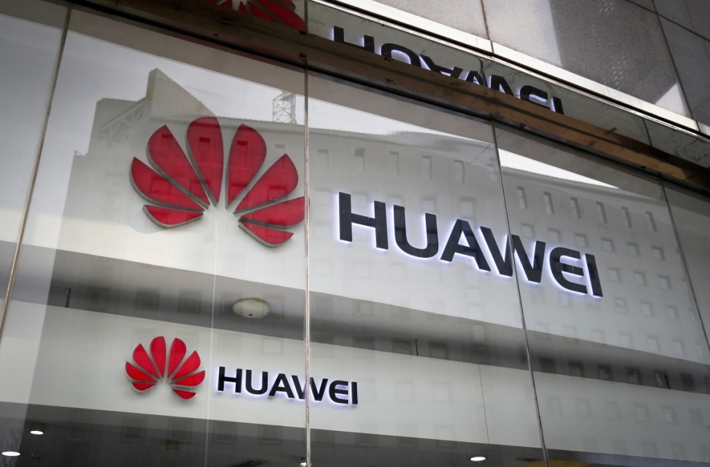 The logos of Huawei are displayed at its retail shop window reflecting the Ministry of Foreign Affairs office in Beijing.