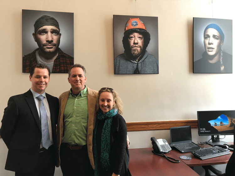 The Senate president’s Chief of Staff BJ McCollister, Hopper McDonough and Heather Perry pose in front of shipbuilder portraits hanging at the state house. 